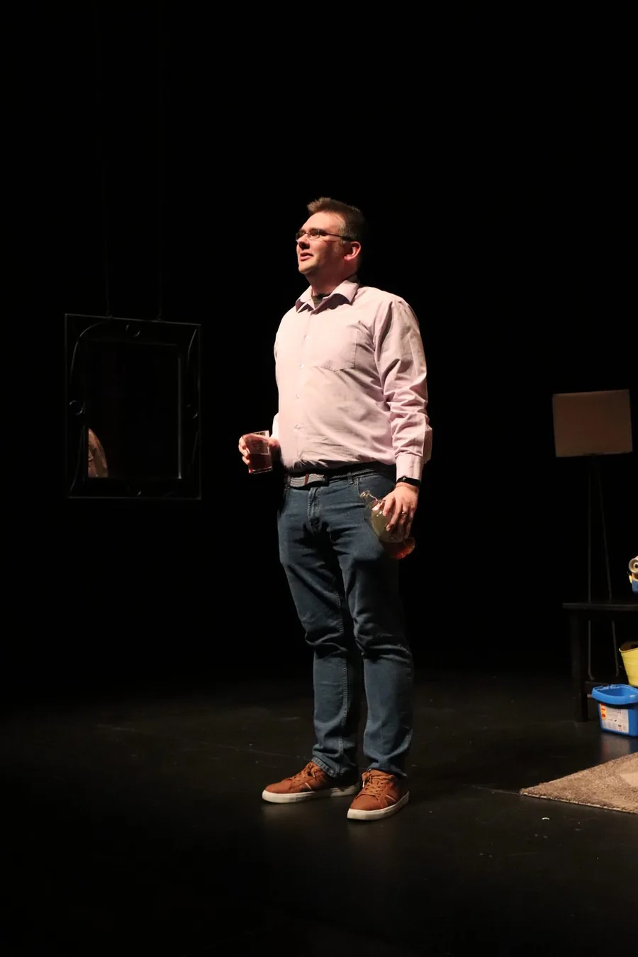 Matthew McMahon performing as David in The Flowers of May, alone in a spotlight holding a glass and a bottle