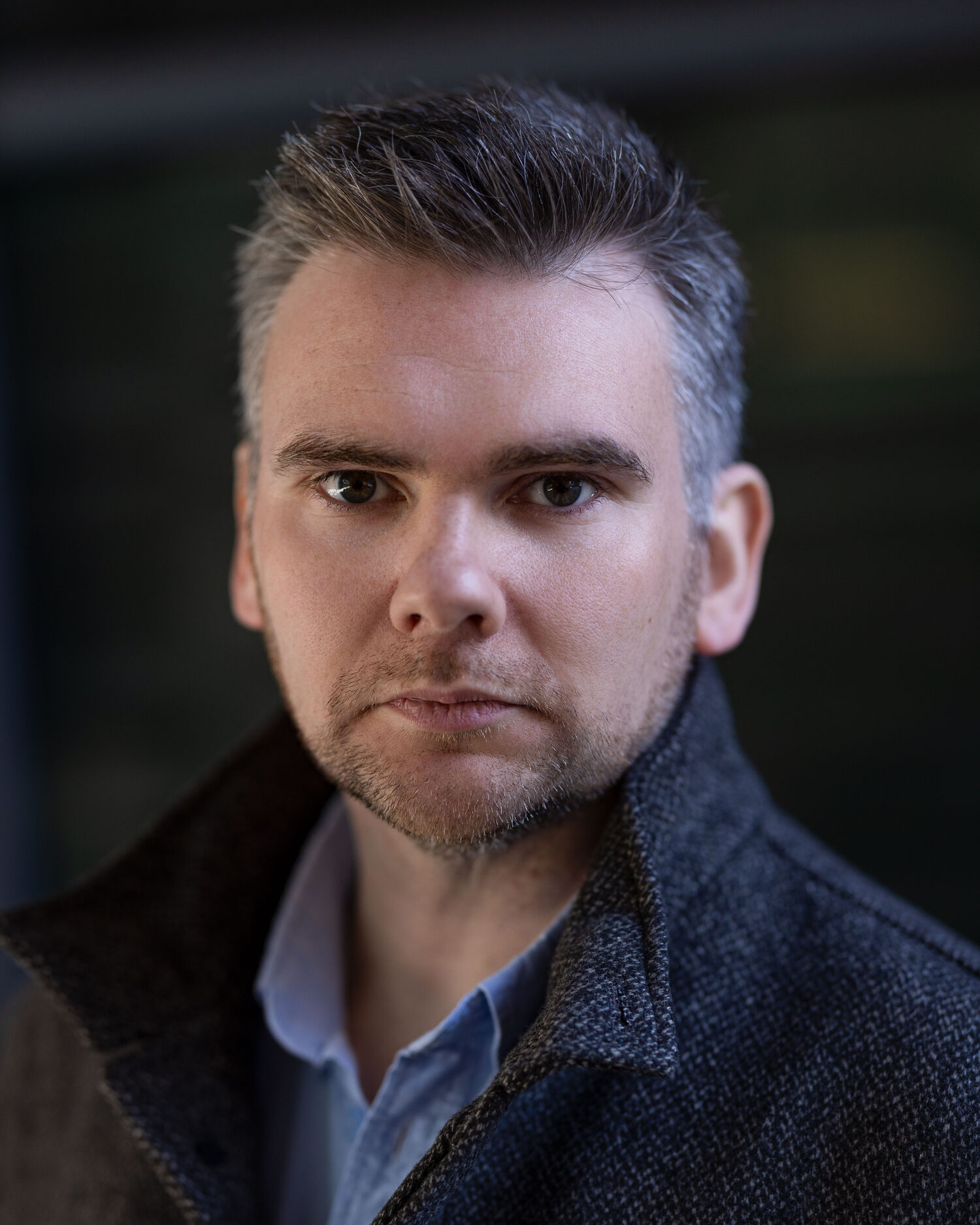 Headshot of Matthew McMahon in a grey wool coat against a dark exterior background